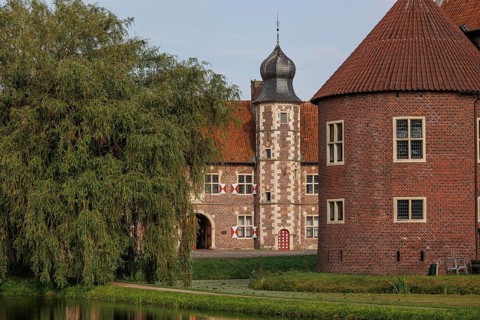 Historic ensemble of buildings with round tower and moat, surrounded by greenery, Raesfeld,