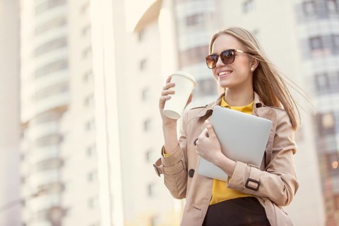 Beautiful young businesswoman with a disposable coffee cup, drinking coffee and holding a tablet in