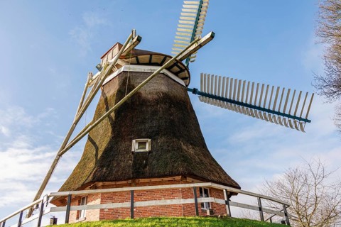 Traditional windmill with thatched roof and wooden construction under a clear blue sky, burlage,