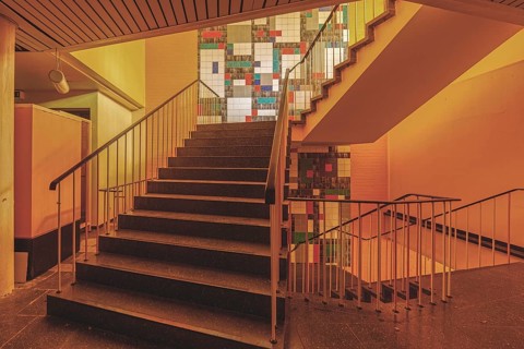 Interior with a staircase and railings, illuminated by yellowish light and with wall art, Bad am