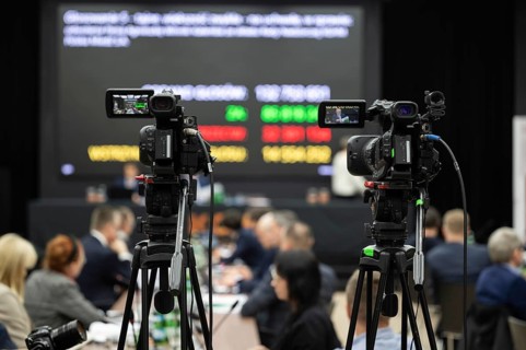 Camera during shareholders' meeting with big screen in the background