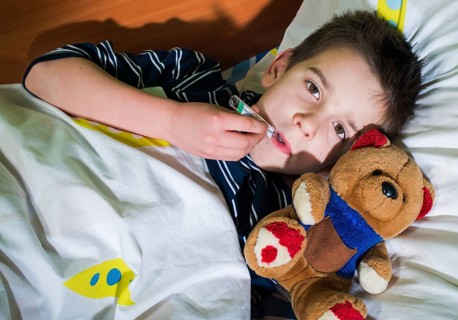 Sick child in bed with teddy bear. Measuring the temperature with a thermometer