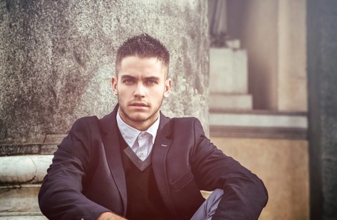 Handsome young man outdoor wearing jacket and shirt standing by historic building in European city.