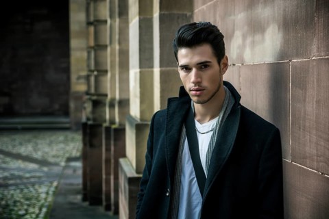 Handsome young man outdoor in winter fashion, wearing black coat and woolen scarf against historic