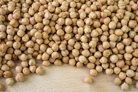 Lot of whole fresh tan chickpea on wooden cutting board. Legumes