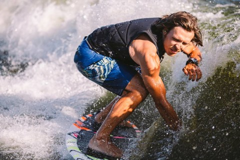 Young athletic man with long hair wakesurfing on waves of river in sunny summer weather. Ttheme