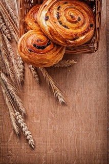 Wicker basket with raisin pastry wheat ears on oaken wooden board food and drink concept