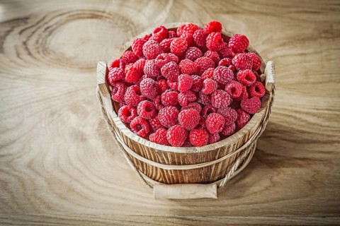 Bucket with raspberries on wooden board