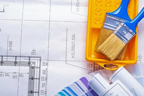 Two paintbrushes in paint can with rolled blueprints on color sampler with copyspace