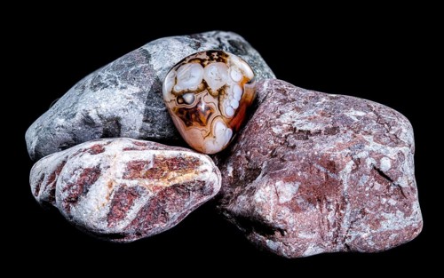 A smooth, polished agate gemstone with intricate banding patterns rests on a group of textured,