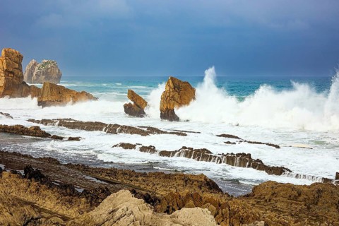 Storm waves break on the coastal rocks. Snow-white sea foam glistens in the dim autumn sun.