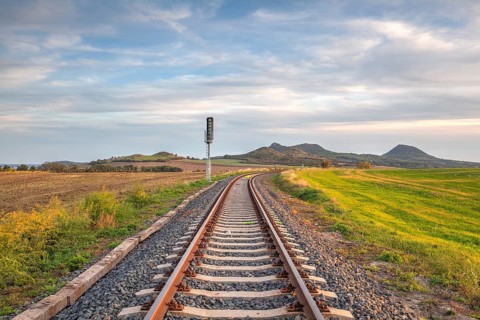 Old Railway tracks running through a field stretch to rural countryside at sunset. Single railway
