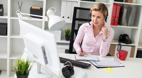A young girl in headphones sits at a table in the office, holds a pencil in her hand and works with