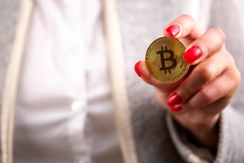 Virtual cryptocurrency money Bitcoin golden coin in the left hand of a woman with red nail polish.