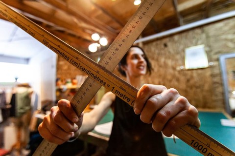 A closeup view of two wood measuring rods being held by a woman tailor inside her retro studio.