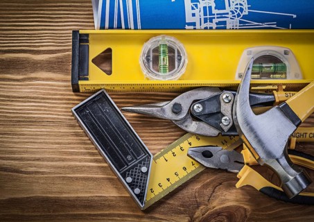 Blue blueprints construction level try square claw hammer pliers tin snips on wooden board