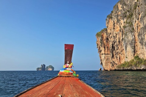 The Thai excursion boat floats to ocean island. The boat nose is decorated by multi-colored and