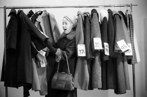 Great discounts of outerwear in the 1960s. A woman stands by a clothes rack, choosing from
