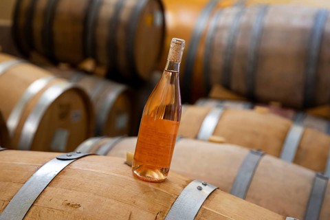A bottle of rose wine on Oak Barrels wine fermenters in a winery
