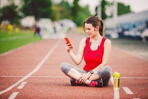 Beautiful fitneß girl uses smartphone at stadium after workout. Sports and healthy. Sport woman use