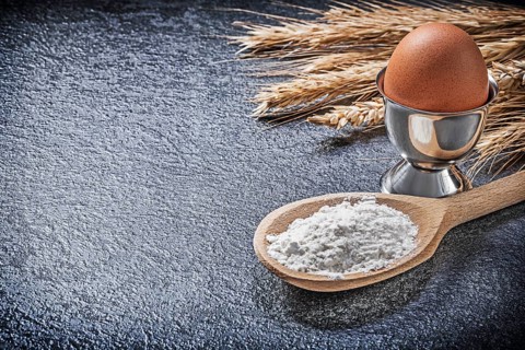 Wheat rye ears wooden spoon flour eggcup boiled egg on black background