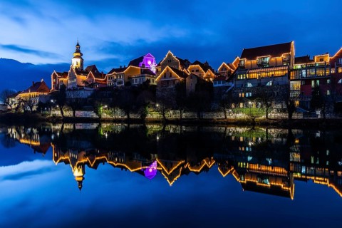 Christmas illuminated house facade of Frohnleiten reflected in the river Mur, blue hour,
