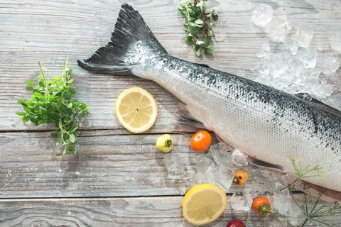Raw salmon fish in ice and vegetables on white table. Baking paper