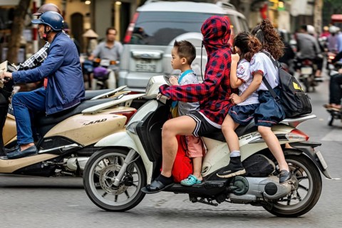 A person with children on a motorbike in a busy city street, woman with children on a scooter in