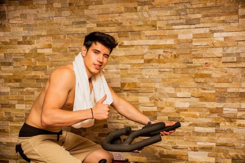 Attractive young man exercising in gym: spinning on stationary bike
