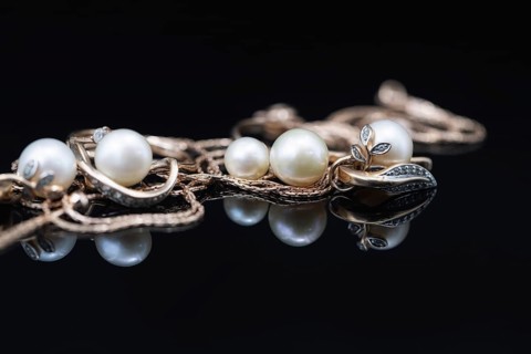 Gold earrings and rings with white pearls lie on a black mirror surface