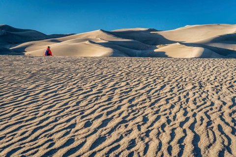 Lost in the sea of sand - a lonely hiker in a dunefield in Great Sand Dunes National Park, Colorado
