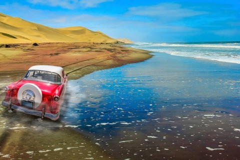 A vintage pink car on a sandy road with dunes and ocean background. Back view of a car. Copy space