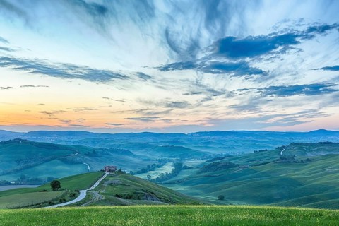 Italian valley in the dawn light with a farm on a hill