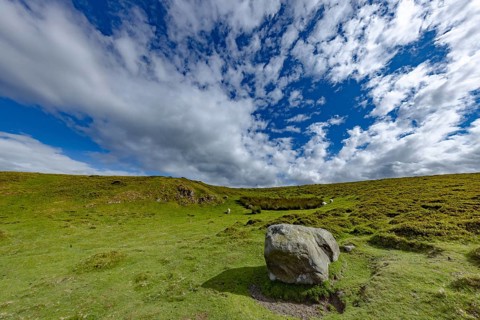 Vast rolling mountain landscape with a cliff and lush green meadows and dramatic skies on the edge