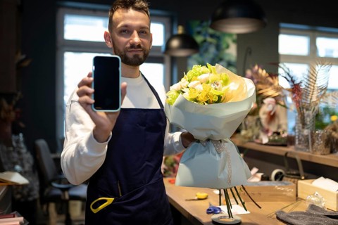 Ein florist mit einem strauß in den händen zeigt den bildschirm eines smartphones vor dem