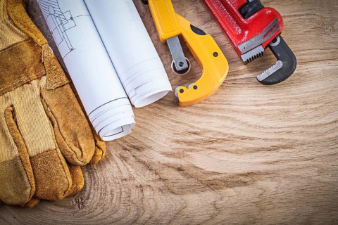 Blueprints protective gloves pipe wrench cutter on wooden board plumbing concept