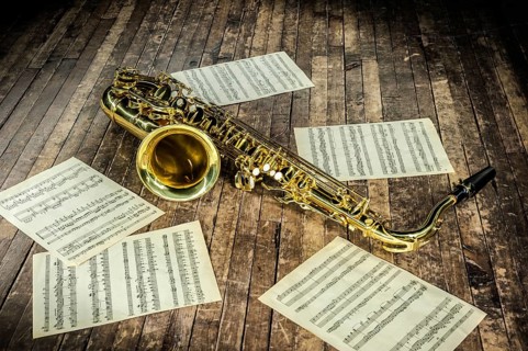 Beautiful yellow saxophone and paper with music score notes lying on a vintage wooden stage