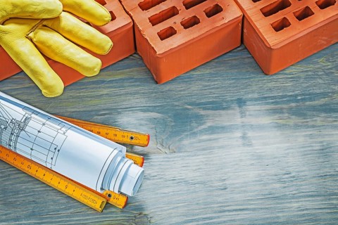 Red bricks leather working gloves construction plans wooden meter on wood board bricklaying concept
