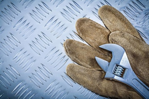 Safety gloves adjustable wrench on grooved metal plate construction concept
