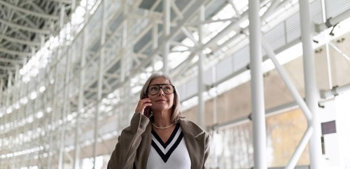 A middle-aged businesswoman with glasses is engaged in a phone conversation while strolling through