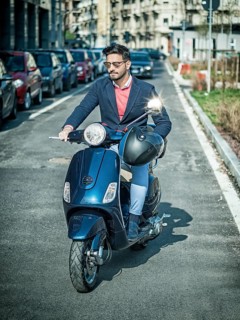 Young stylish man in suit and sunglasses driving scooter on empty road in sunny city