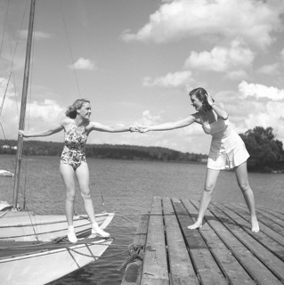 1940s summer. Two young at a marina on a summer's day. The girl getting from the boat onto the