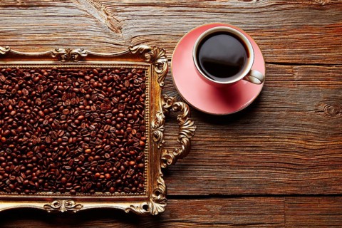 Coffee cup and beans on vintage golden tray in wooden old table
