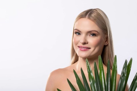 A smiling woman poses with a vibrant tropical plant against a soft light backdrop, showcasing