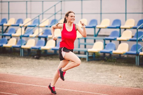 Female runner jogging on stadium track, woman athlete running and working out outdoors, sport and