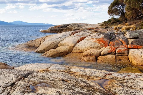 Granite boulders reddened by lichens are polished smooth by waves, Swansea, Tasmania, Australia,