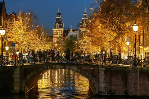 Bicycles parked on a night-lit bridge over a canal, Amsterdam, Netherlands