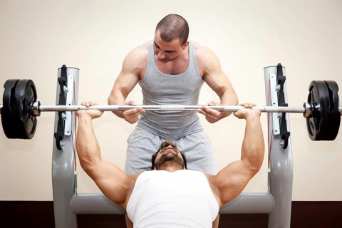 A handsome young muscular sports man doing bench press with a little help