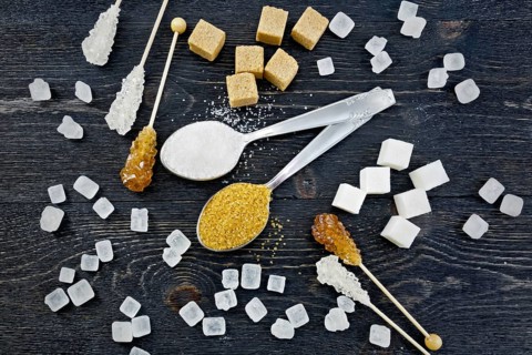 Sugar white and brown granulated in spoons, crystal and cubes on the background of a black wooden