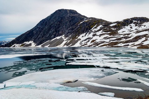 The very cold clear water of the lake Djupvatnet is covered with ice in July. The mountains are